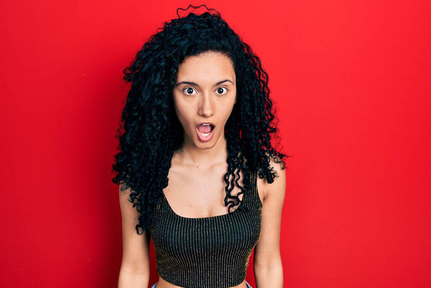 Young hispanic woman with curly hair wearing casual style with sleeveless shirt scared and amazed with open mouth for surprise, disbelief face  - Фото, изображение