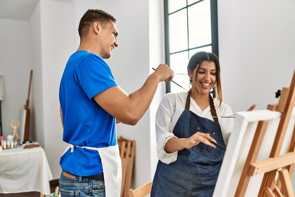Δύο μαθητές χαμογελώντας ευτυχισμένοι παίζοντας με ζωγραφική πινέλο ο ένας στον άλλο στη Σχολή Καλών Τεχνών. - Φωτογραφία, εικόνα