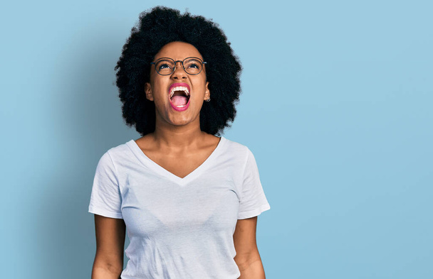 Mladá afrikánská Američanka, oblečená v obyčejné bílé tričko, rozzlobená a šíleně křičící, frustrovaná a zuřivá, křičící vztekem. vztek a agresivní koncept.  - Fotografie, Obrázek