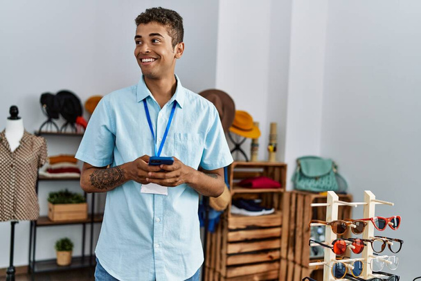 Fiatal spanyol férfi dolgozik, mint bolti asszisztens használ okostelefon a kiskereskedelmi üzletben - Fotó, kép