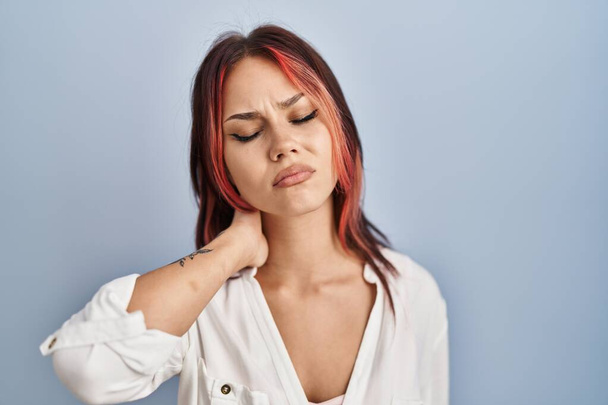Young caucasian woman wearing casual white shirt over isolated background suffering of neck ache injury, touching neck with hand, muscular pain  - 写真・画像