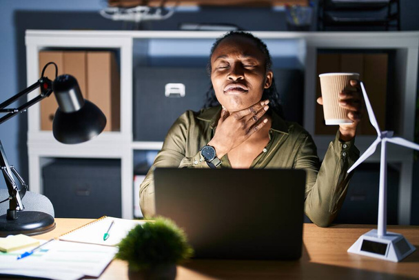 Femme africaine travaillant à l'aide d'un ordinateur portable la nuit en touchant le cou douloureux, mal de gorge pour la grippe, la motte et l'infection  - Photo, image