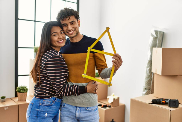 Junges lateinisches Paar lächelt glücklich und hält Hausbau-Projekt in neuem Zuhause. - Foto, Bild