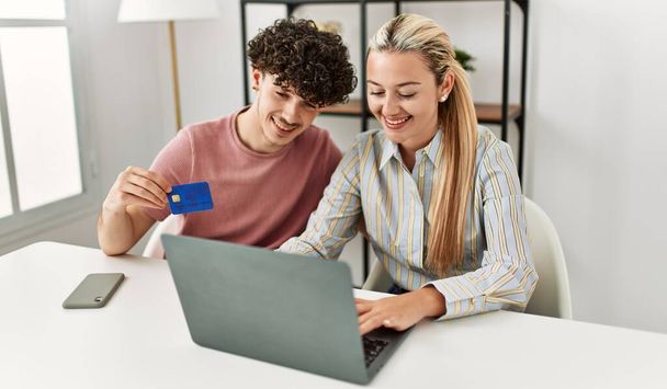 Νεαρό ζευγάρι αγοράζει χρησιμοποιώντας φορητό υπολογιστή και πιστωτική κάρτα στο σπίτι. - Φωτογραφία, εικόνα