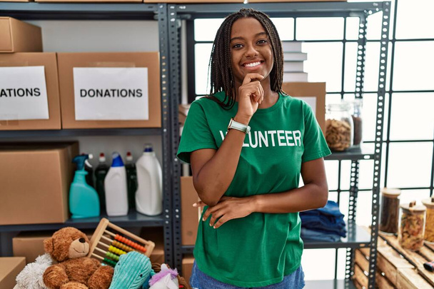 A fiatal afro-amerikai nő, aki önkéntes pólóban dolgozik adománygyűjtésen, állon állva gondolkodik a kérdésen, az elmélkedő arckifejezésen. mosolygós és figyelmes arc. kétség.  - Fotó, kép