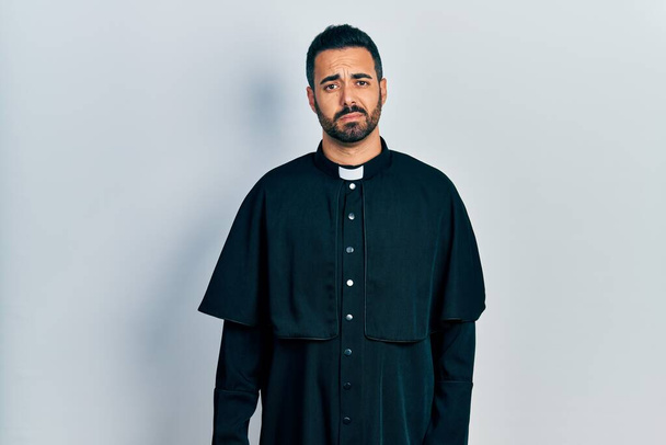 Handsome hispanic man with beard wearing catholic priest robe looking sleepy and tired, exhausted for fatigue and hangover, lazy eyes in the morning.  - Photo, Image