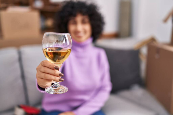 Young middle east woman smiling confident drinking glass of wine at new home - Foto, afbeelding