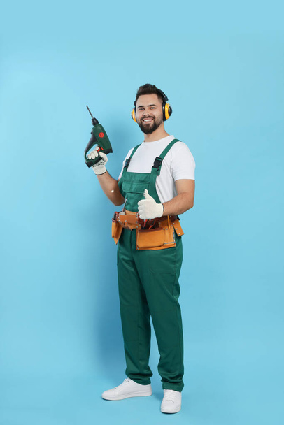 Young worker in uniform with power drill on light blue background - Фото, зображення