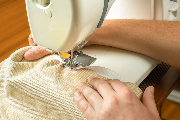 Seamstress hands holding white textile fabric. Male hands stitching white fabric on modern sewing machine at workplace. Close up view of sewing process. Handmade, hobby, small business concept - Photo, Image