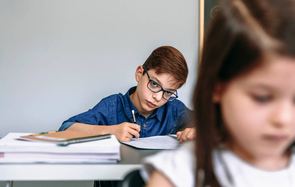 Teen píše do sešitu ve škole. Selektivní zaměření na chlapce v pozadí - Fotografie, Obrázek