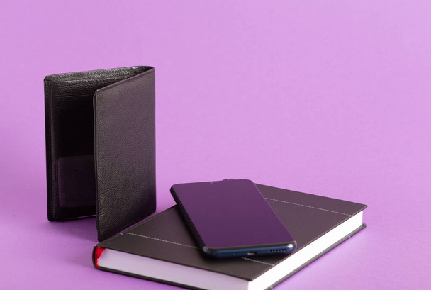 A closeup of a smartphone on a notebook and a wallet on a purple background - 写真・画像