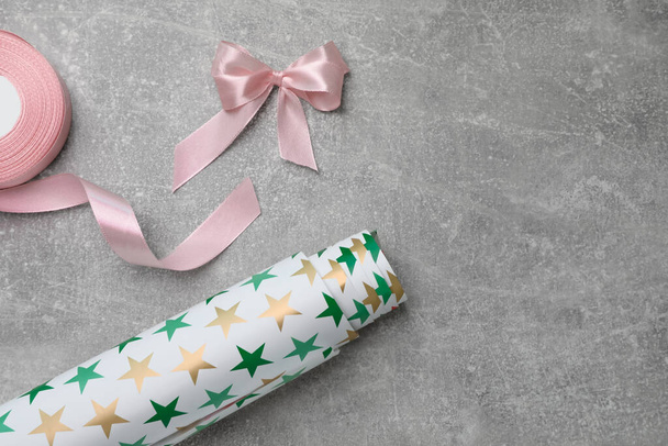 Roll of festive wrapping paper and pink satin ribbon on grey table, flat lay. Space for text - Photo, image