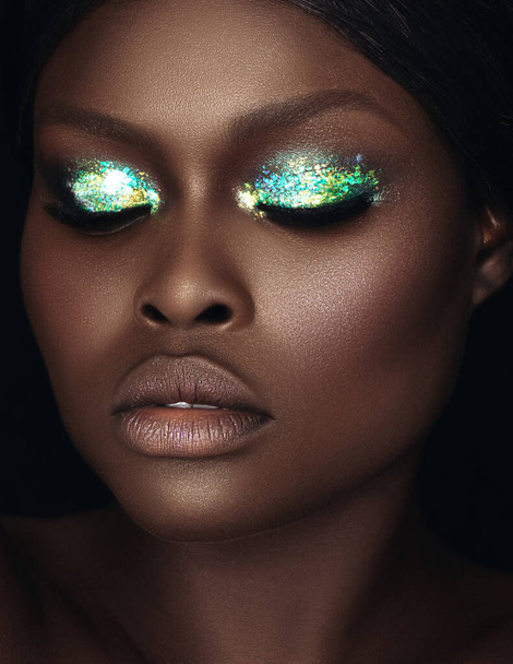 A vertical closeup shot of a Black female with green glitter eye make up - Photo, image