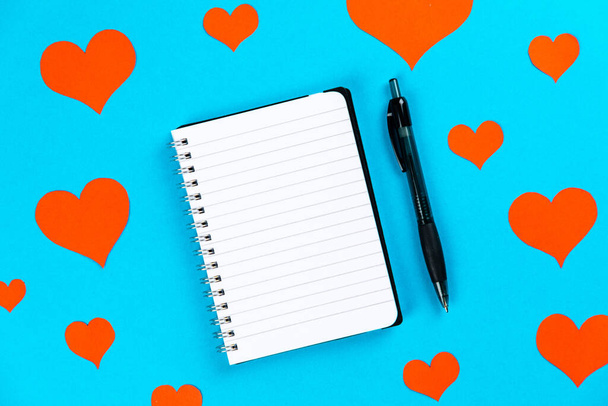 A top view of a notebook with pen on a blue background with red hearts - Valokuva, kuva