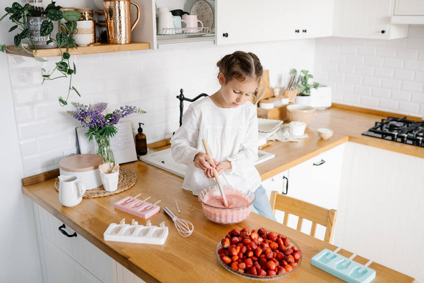 Homemade ice cream. Cute little girl preparing homemade strawberry ice cream at the kitchen. Summer food. - Zdjęcie, obraz