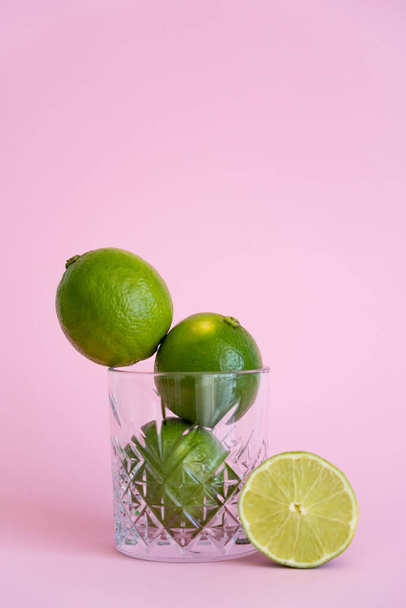 green fresh citrus fruit in faceted glass near half of lime on pink  - Foto, Imagen