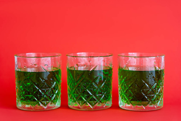 green alcohol drink in three faceted glasses with water drops on red - Foto, Imagen