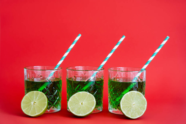 green alcohol drink in faceted glasses with straws and halves of limes on red - Foto, Bild