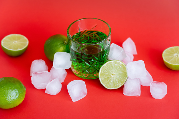 замороженные кубики льда возле стекла с алкогольным мохито и свежими лаймами на красном - Фото, изображение