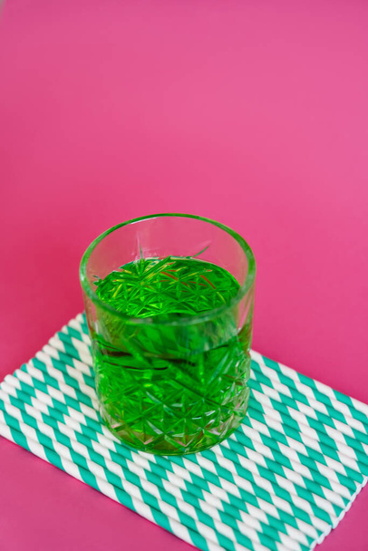 high angle view of glass of green alcohol drink on striped paper straws on pink - Photo, Image