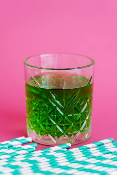 striped paper straws near faceted glass with green cocktail on pink - Fotoğraf, Görsel