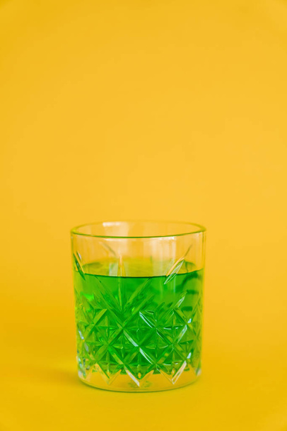 faceted glass with green alcohol drink on yellow - Foto, afbeelding