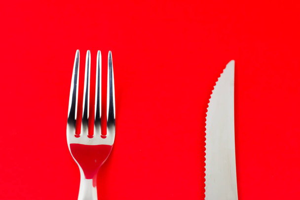 A top shot of silver fork and a knife on a bright red background. - 写真・画像