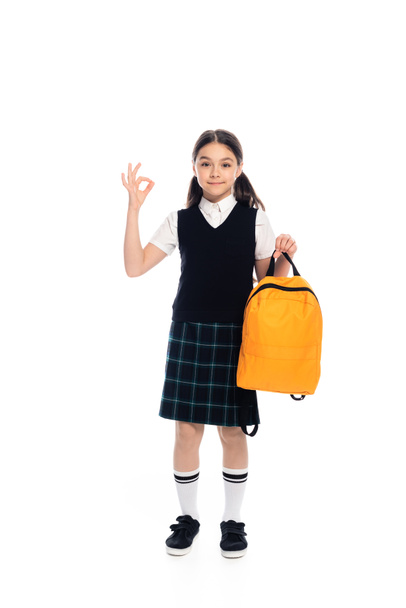 Full length of pupil showing ok gesture and holding backpack on white background - Foto, Imagem