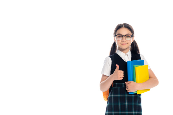 Pupil in eyeglasses holding books and showing thumb up isolated on white  - Foto, imagen