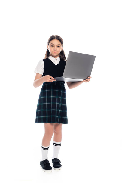 Full length of schoolkid in skirt holding laptop on white background - Фото, изображение