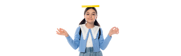 Positives Schulkind mit Buch auf dem Kopf und Rucksack mit Mudra-Geste auf weißem Banner  - Foto, Bild
