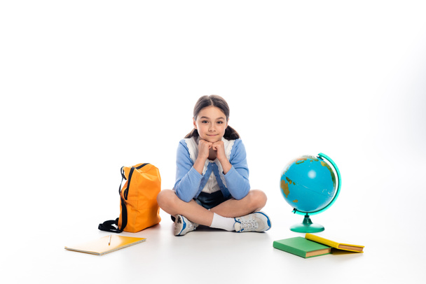 Preteen schoolchild looking at camera near backpack and globe on white background - Photo, Image