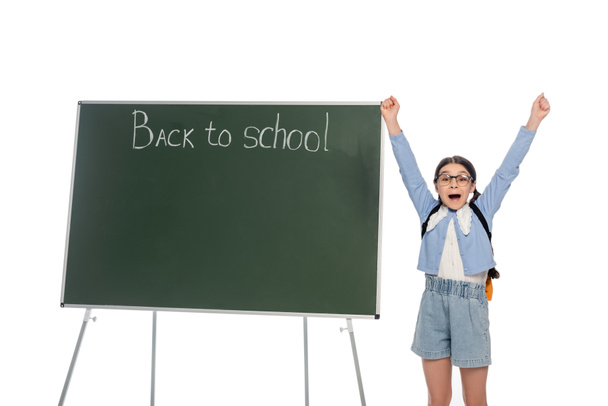 Excited pupil showing yes gesture near chalkboard with back to school lettering isolated on white  - Foto, Imagem