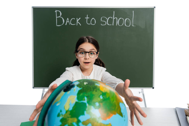 Nadšený školačka natahuje ruce na zeměkouli v blízkosti tabuli s zpět do školy písmo izolované na bílém  - Fotografie, Obrázek