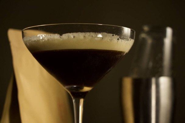 A closeup shot of an espresso martini cocktail with shaker and coffee bag in the blurred background - Photo, image