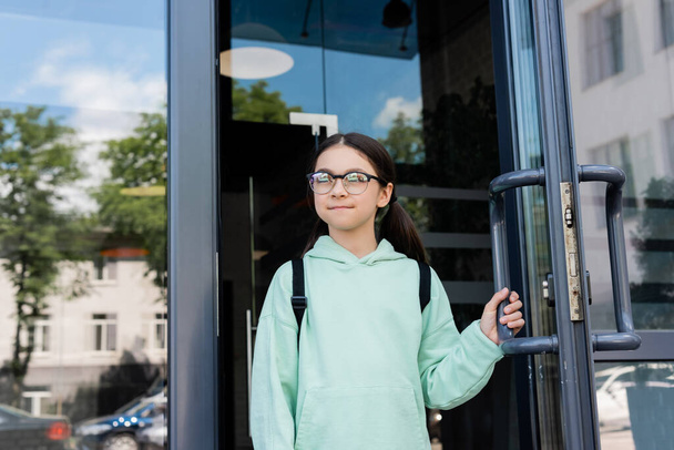 Uczeń z plecakiem otwierającym drzwi budynku na zewnątrz  - Zdjęcie, obraz