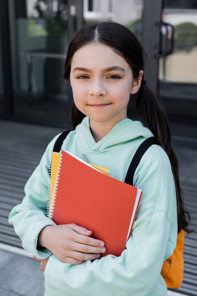 Portrait of schoolkid holding notebooks outdoors  - Фото, изображение