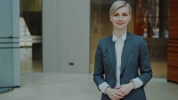 Portrait of successful blonde businesswoman smiling and looking into camera in modern office indoors - Foto, Imagen