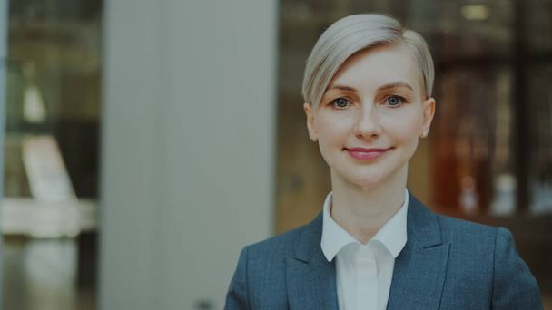 Close-up portrait of successful blonde businesswoman smiling and looking into camera in modern office indoors - Foto, Imagen