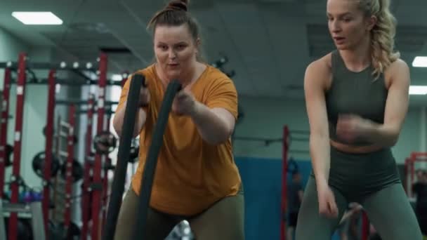Kilolu bir kadın savaş halatlarıyla egzersiz yapıyor ve spor salonunda kadın eğitmen. 4K 'da kırmızı helyum kamerayla çekildi..   - Video, Çekim
