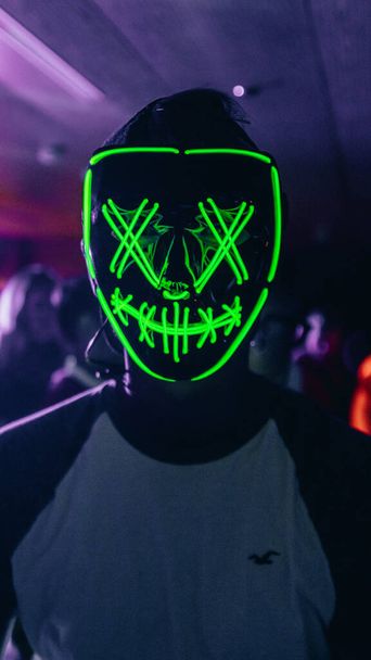 Вертикальный снимок человека в зеленой неоновой маске на вечеринке в клубе - Фото, изображение