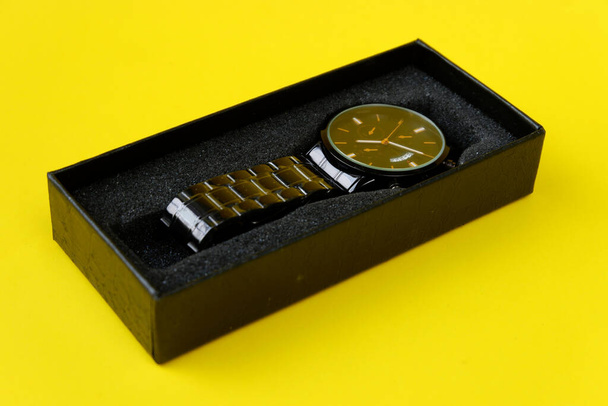 A closeup shot of a luxury wristwatch on a black gift box against a yellow background - Foto, Imagen