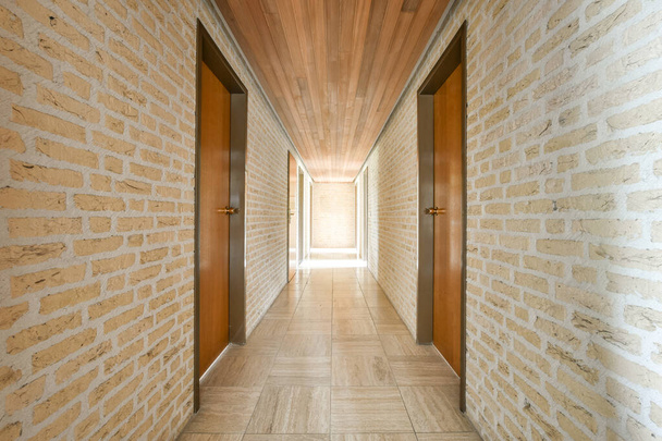 Светлый узкий коридор с множеством дверей в кирпичных стенах и паркетном полу - Фото, изображение