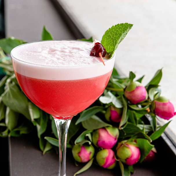 Elegante cocktail da donna rosso con schiuma rosa in un bel bicchiere su una tavola rotonda intagliata in legno. - Foto, immagini