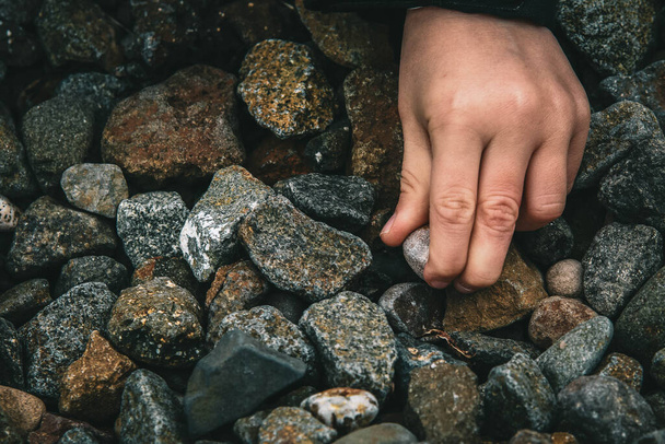 A closeup shot of an adult hand picking up a small gravel off the ground during daytime - 写真・画像