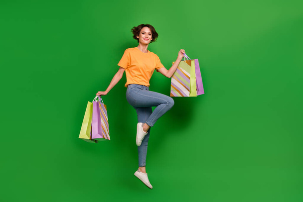 Full length photo of active overjoyed person jump arms hold packages isolated on green color background. - Фото, зображення