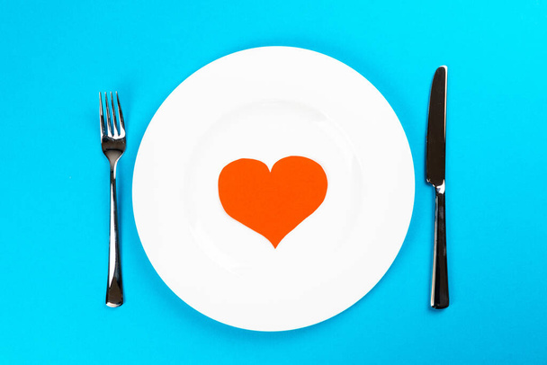 A top view of a white plate with blue background and red hearts for valentines dinner - Valokuva, kuva