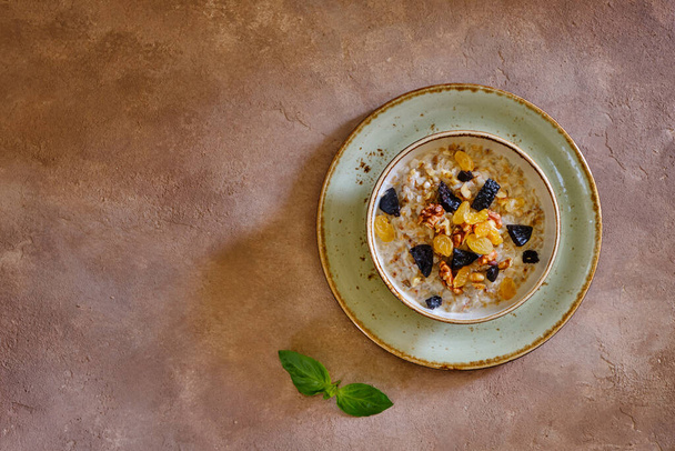 Buckwheat porridge with walnut, raisins and prunes on a green plate on a brown background under concrete. Delicious and healthy - Foto, Imagem