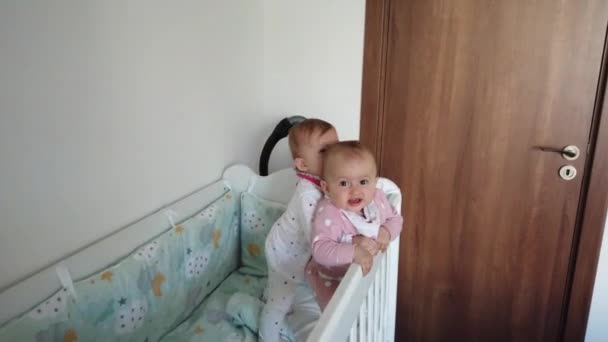 Zwei brüderliche Zwillingsschwestern haben ihren Spaß in der Krippe. Zwei Babys im Kinderbett. - Filmmaterial, Video