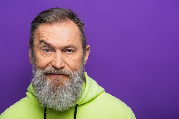 skeptical senior man moving eyebrow while looking at camera on purple background  - 写真・画像